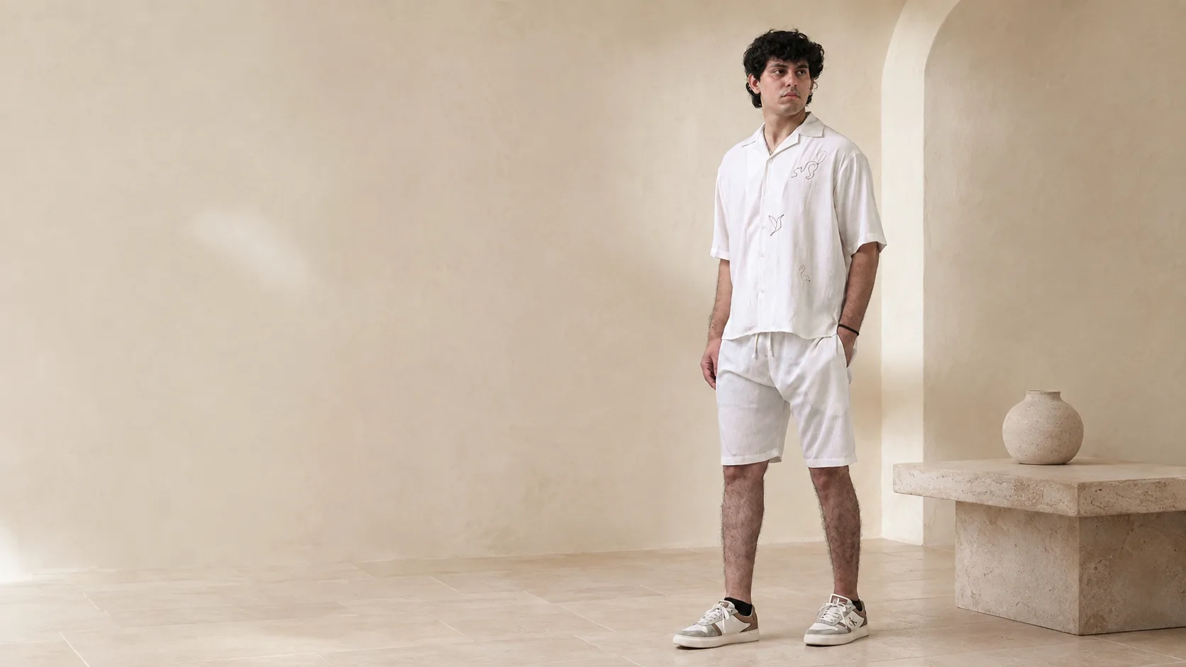 Model wearing the RIZONÉ line art camp collar shirt with white drawcord shorts in a stone courtyard